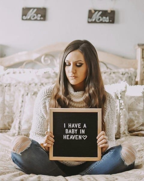 woman sitting on a bed with a letterboard announcing her miscarriage
