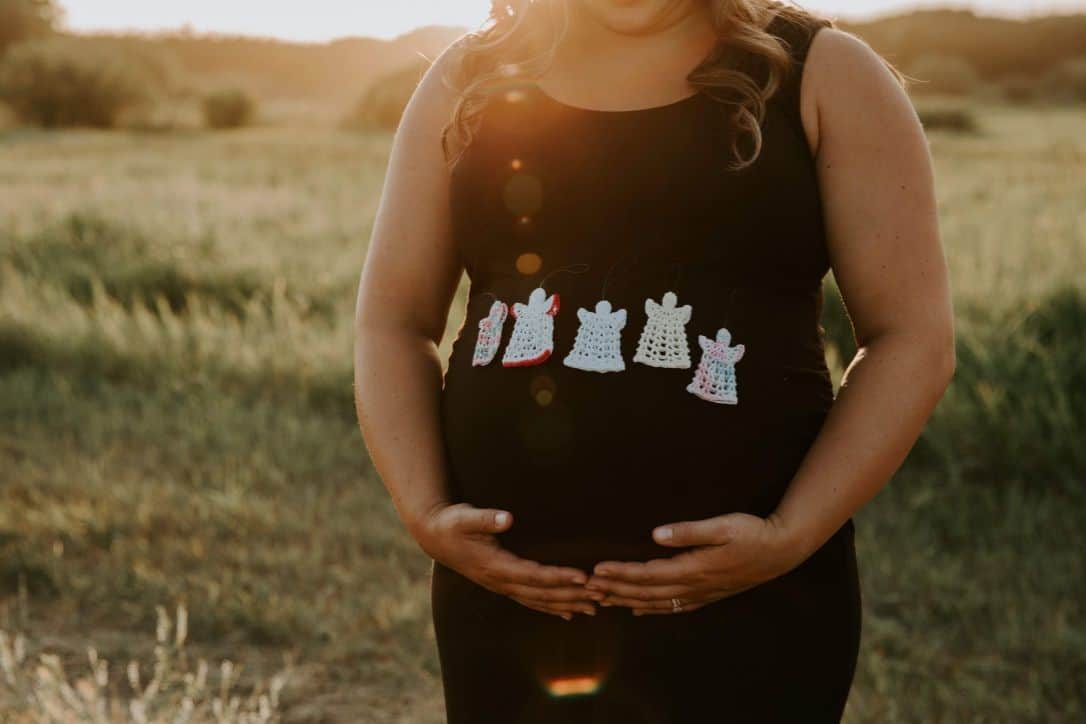 woman holding her pregnant belly with crocheted angels on her shirt that she received as miscarriage gifts
