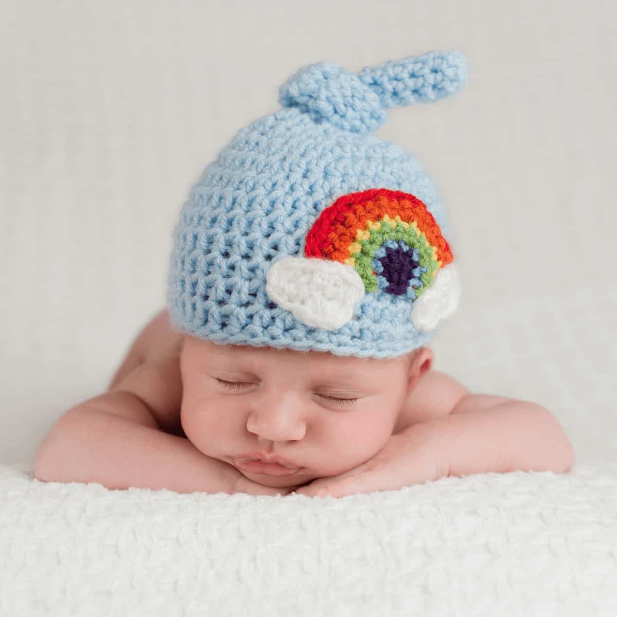 Infant baby is wearing a crochet hat that includes a rainbow design