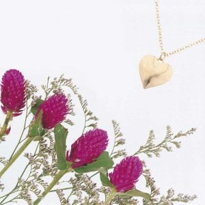 flat-lay-photo-of-pinkish-purple-flowers-in-the-bottom-left-corner-and-a-golden-heart-shaped-necklace-in-the-upper-right-corner-meant-to-show-2-healing-gifts-for-miscarriage