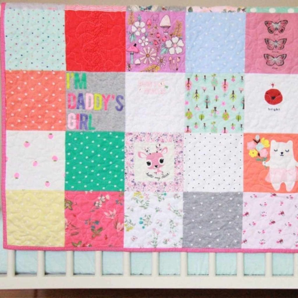 quilt made out of different onesies hanging on a crib with a pink border