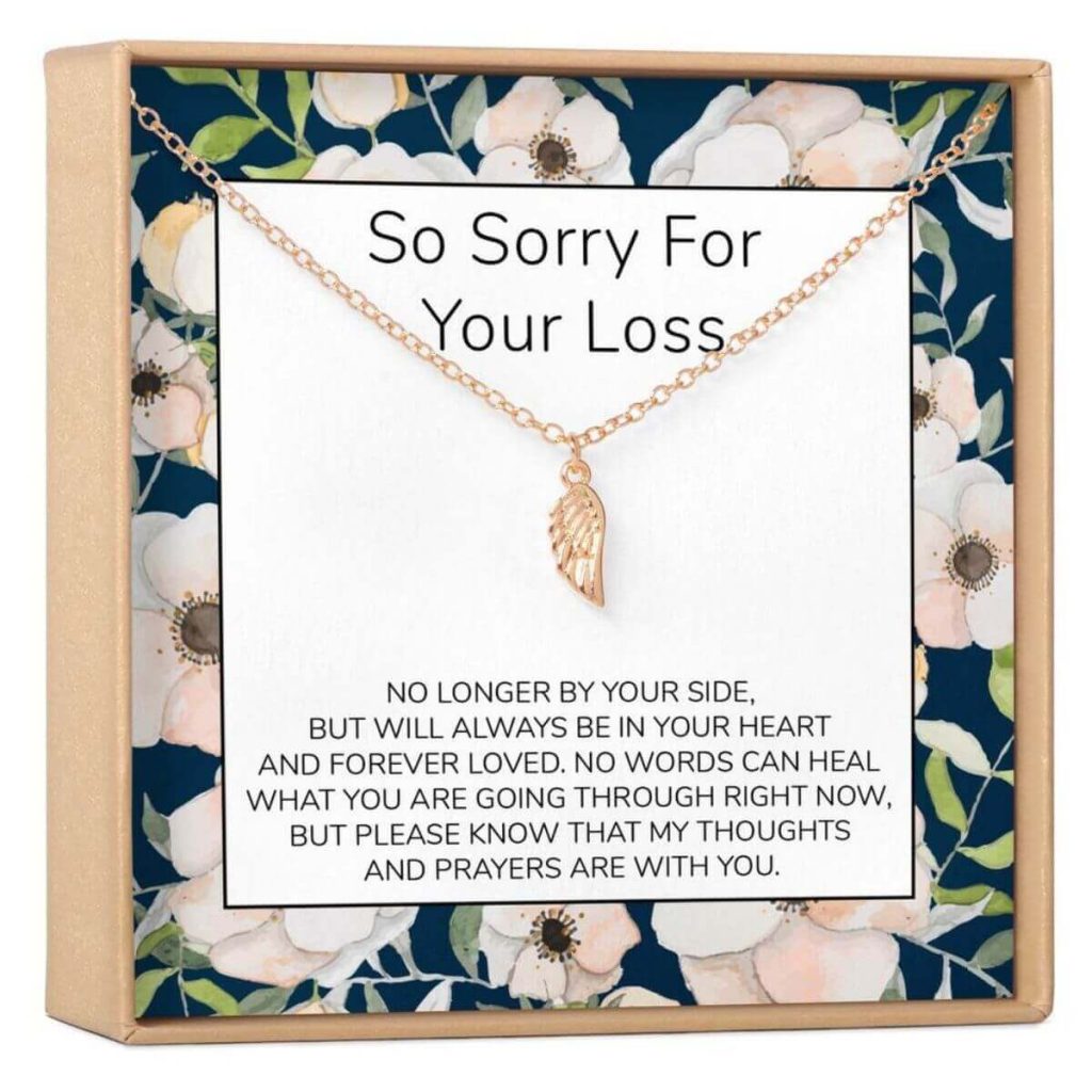gold necklace with dainty angel wing pendant on a floral rimmed piece of cardboard that says so sorry for your loss
