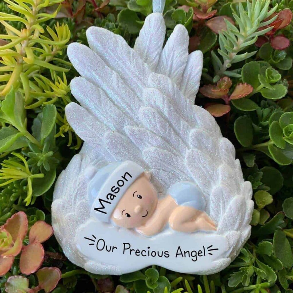 white angel wing miscarriage christmas ornament hanging on tree with figure of little baby that says our precious angel