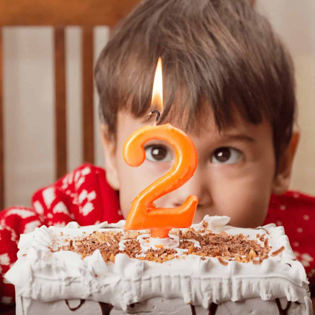 2-year-old-bo2 year old boy crouching behind birthday cake with a lit number 2 candley-crouching-behind-birthday-cake-with-a-lit-number-2-candle
