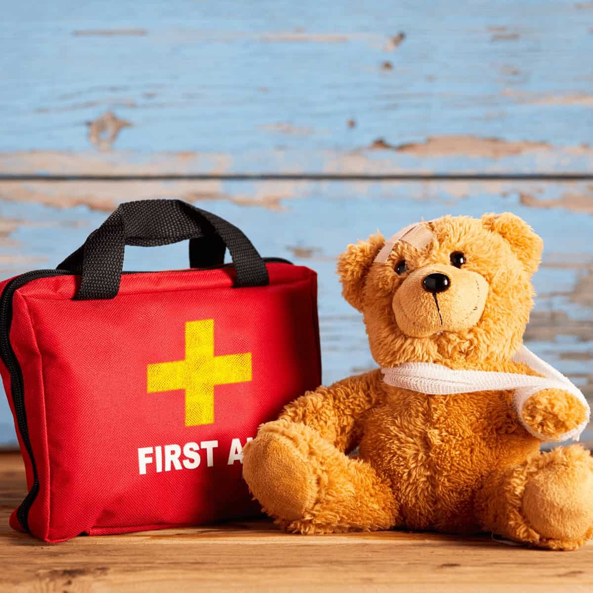 brown-teddy-bear-in-front-of-blue-wall-sitting-next-to-first-aid-kit