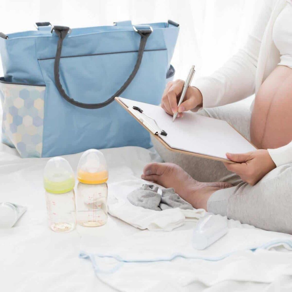 pregnant woman sitting on bed with baby items making her hospital bag checklist
