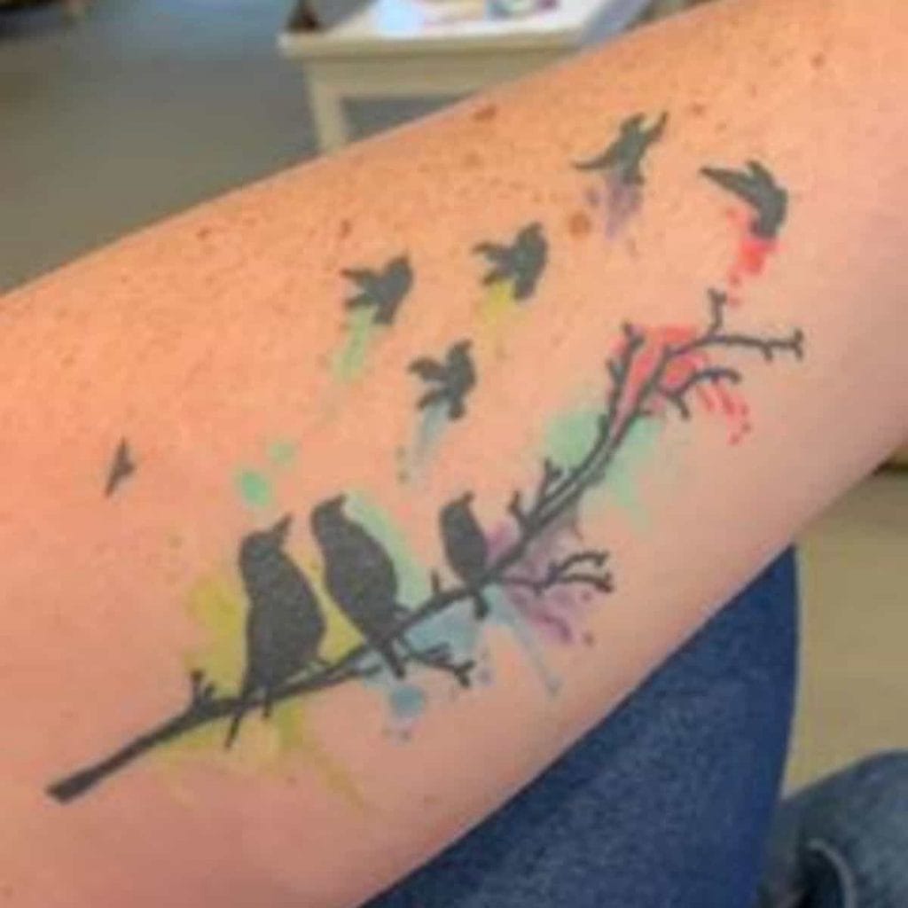 miscarriage tattoo of watercolor of birds with birds on the branch representing living family members and birds flying away representing babies lost to miscarriage