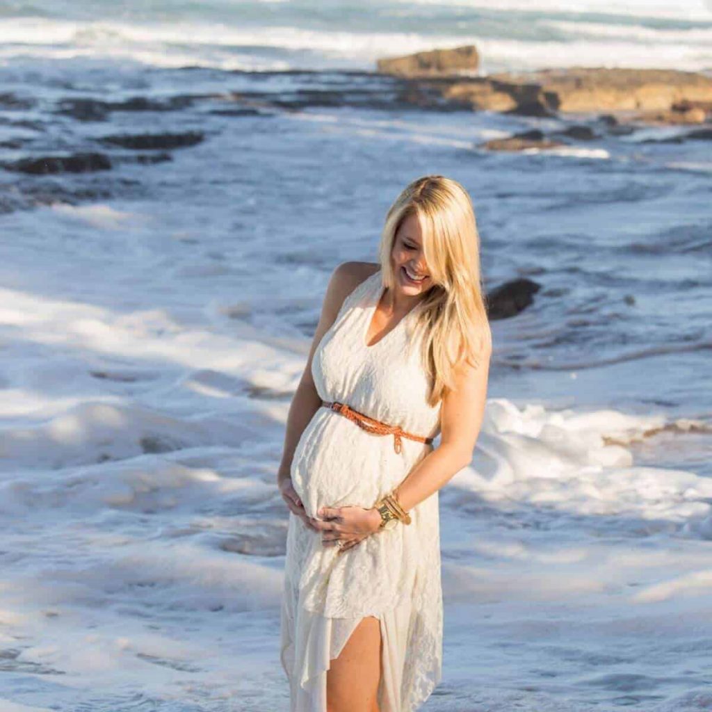 blonde pregnant woman holds her belly on the beach