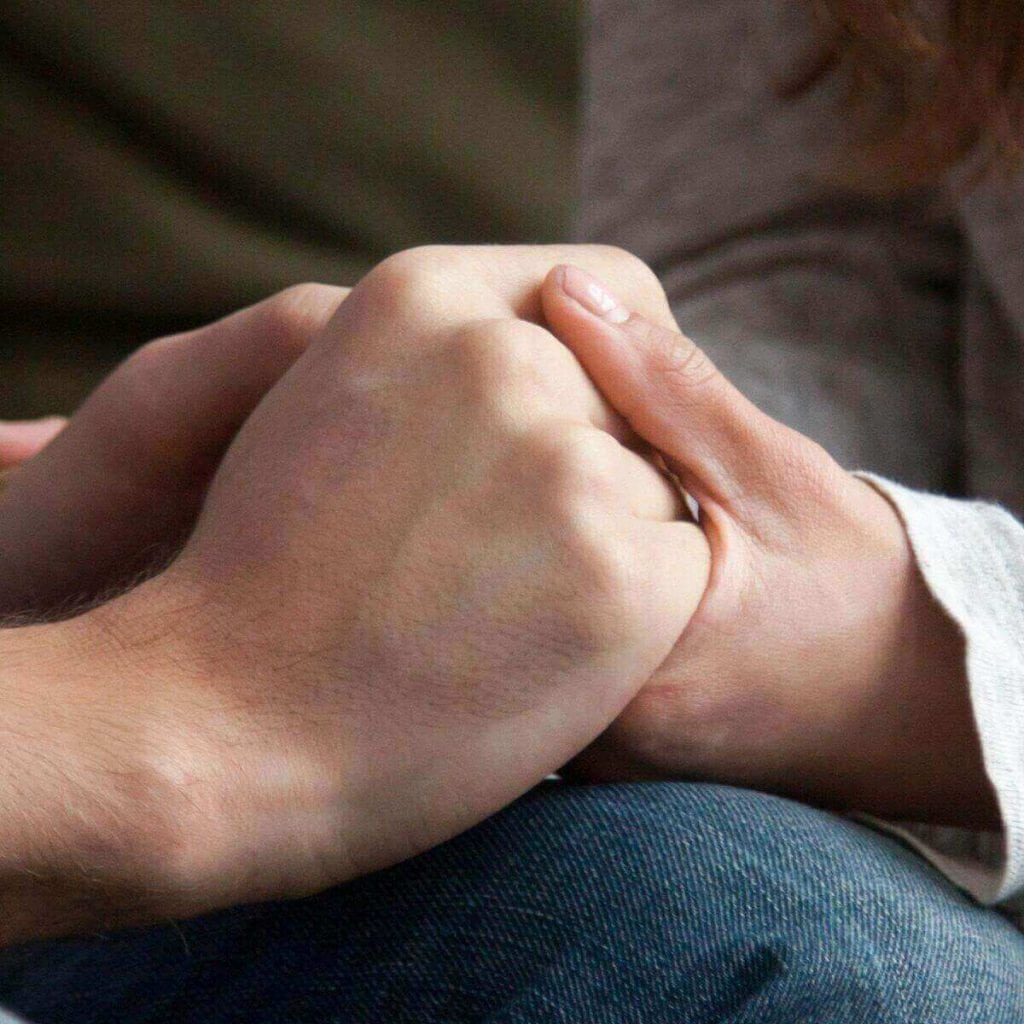 Closeup shot of hands of a man and woman, holding each other while grieving cancelled IVF appointment