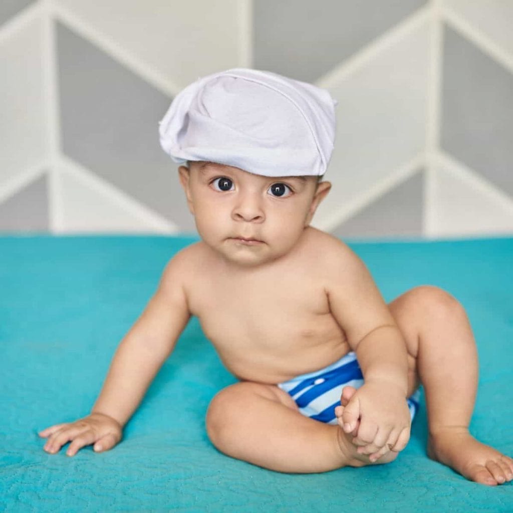 precious baby in white hat in a blue and white cloth diaper