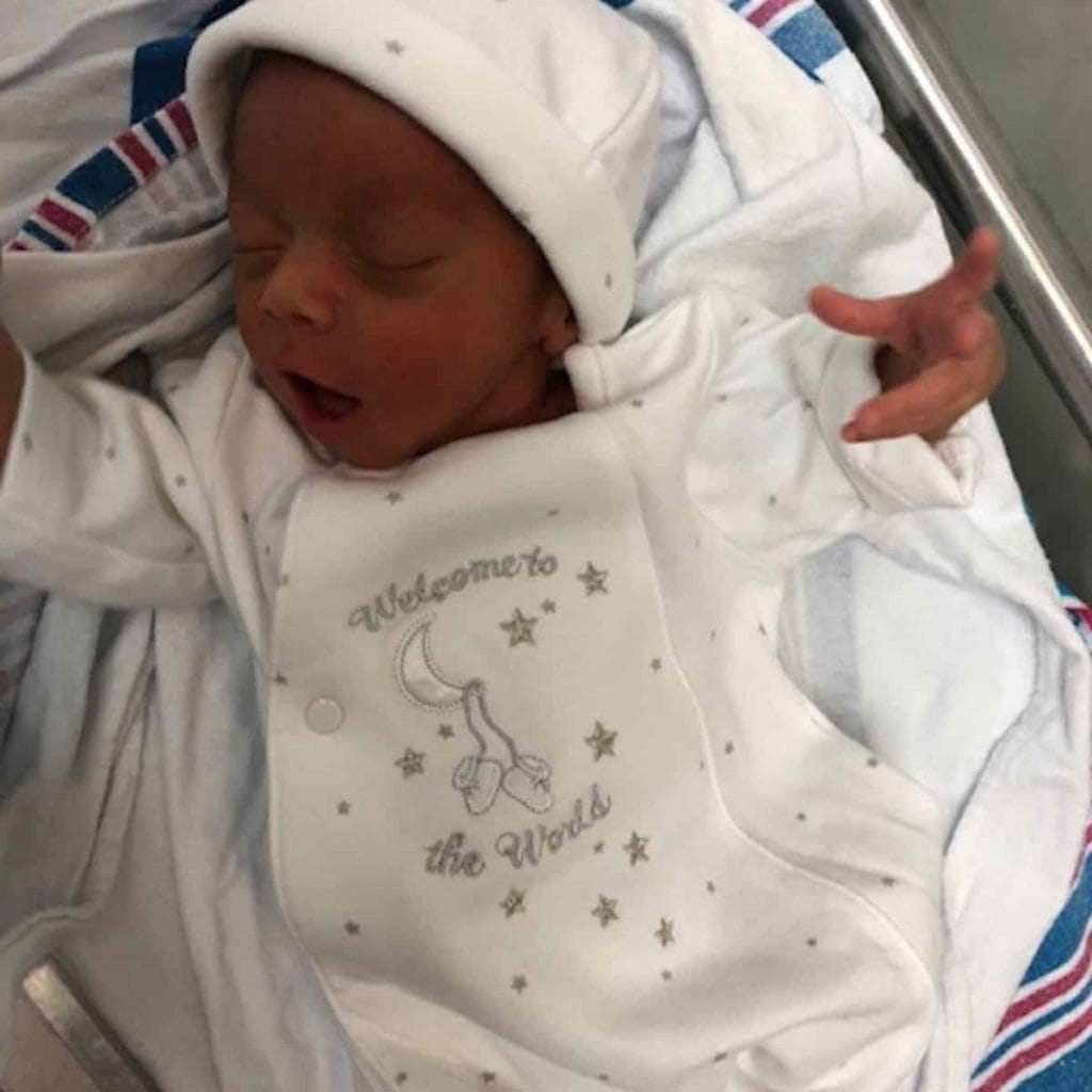 tiny baby in white outfit yawns during his stay in the NICU