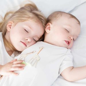Baby and toddler snuggling on bed in soft white pajamas