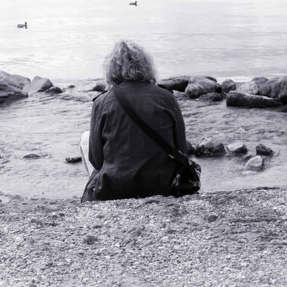 black and white photo of a woman sitting on the beach with her back facing the camera