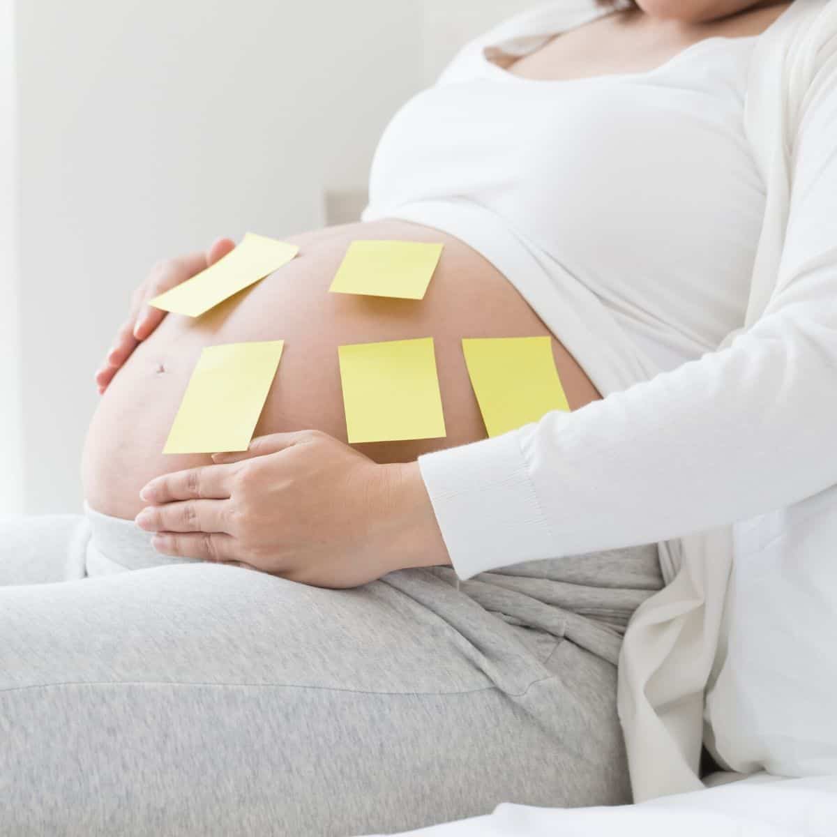 pregnant woman has sticky notes attached to her belly, showing that she's trying to decide on a baby name