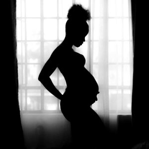 black and white silhouette photo of a pregnant black woman holding her stomach