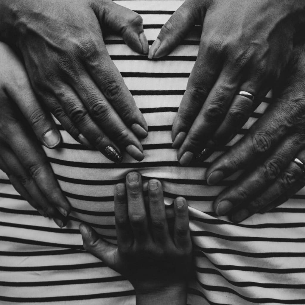 black and white photo of a mother, father, and child holding their hands on the mother's pregnant stomach
