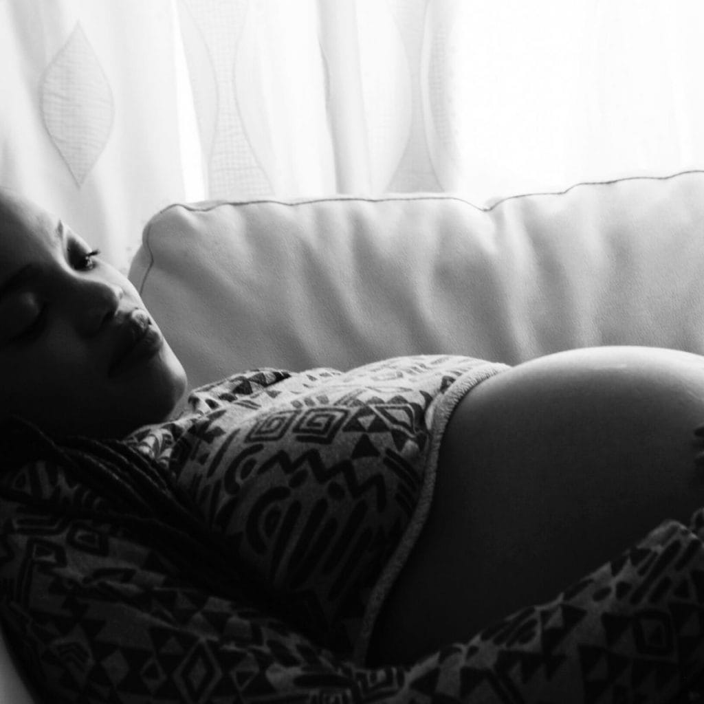 black and white photo of a black pregnant woman looking down at her stomach while laying on a couch