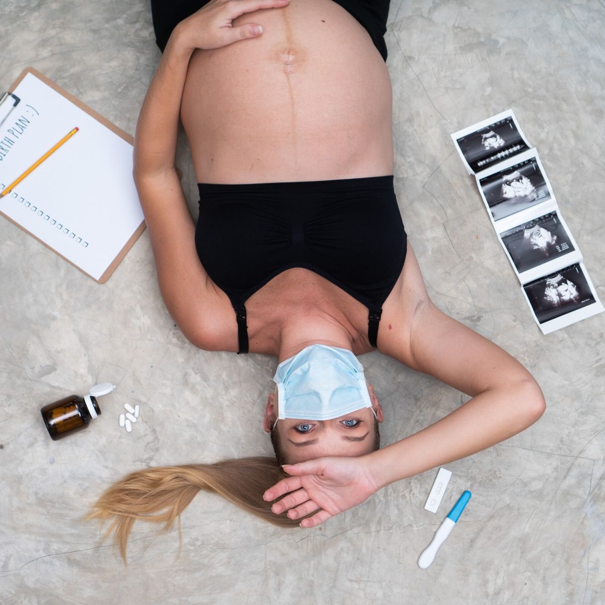 pregnancy woman wearing a face mask with a pregnancy test, sonogram, and birth plan notes laying near her