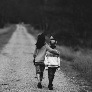 black and white photo of young girl putting her arm around a young boy while they walk down a dirt road