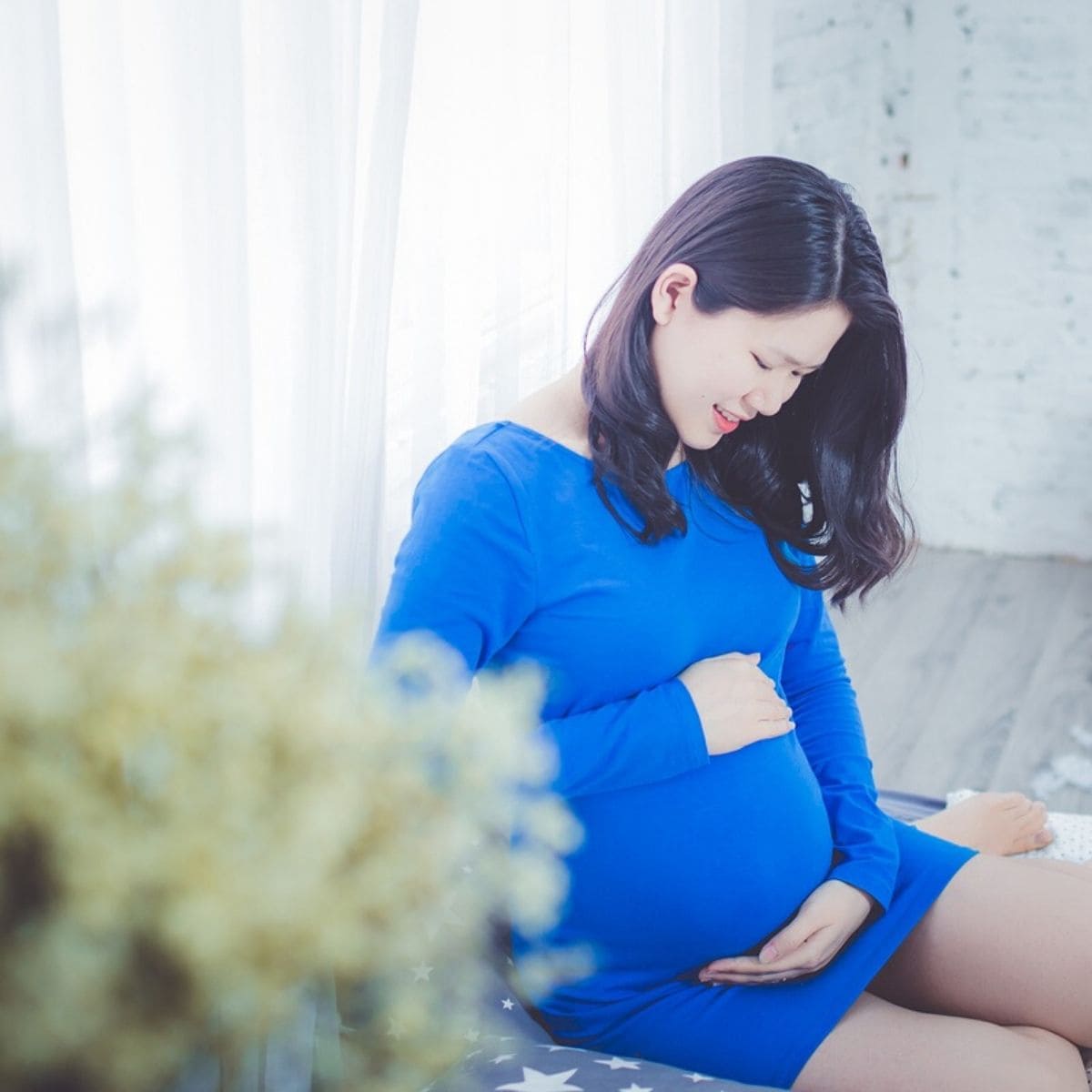 pregnant woman is wearing a blue dress and looking down at her pregnant belly