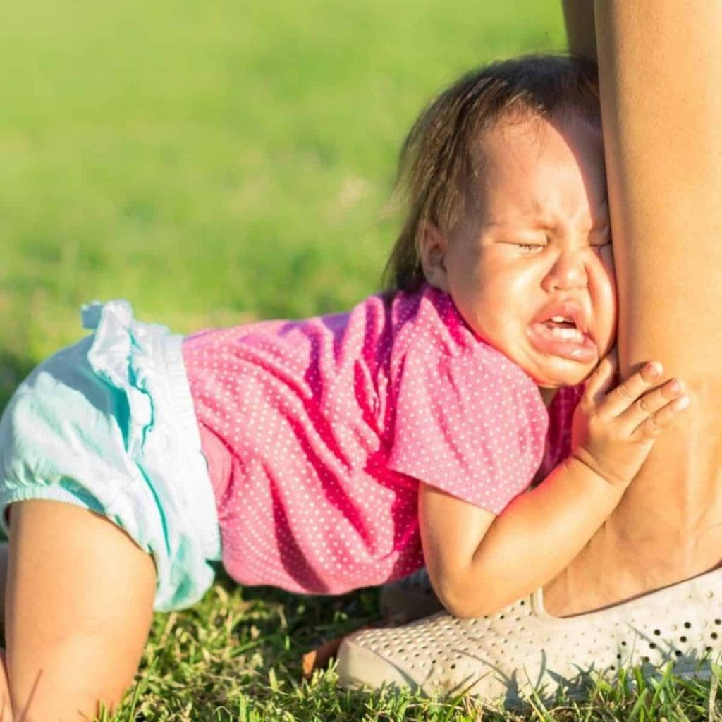 crying toddler holding on to her mother's ankle