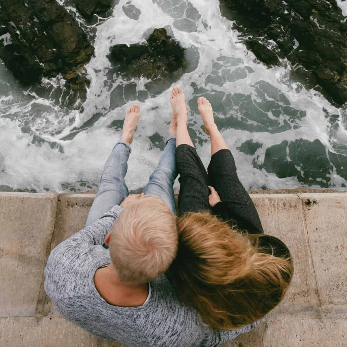 couple hold each other close while sitting on the edge of the ocean