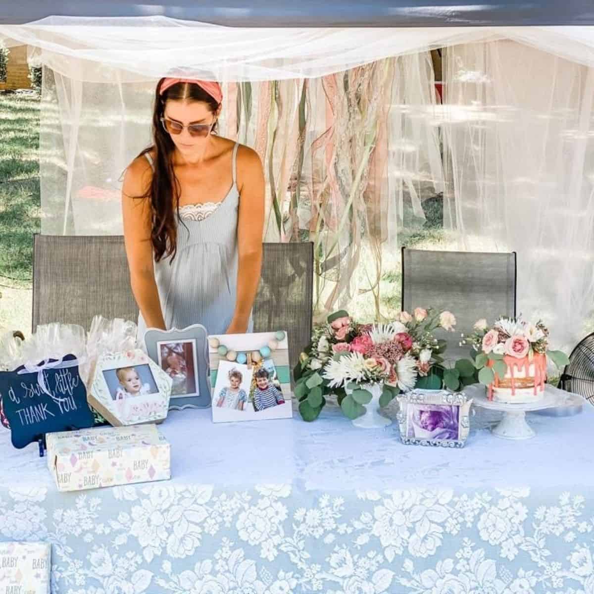 woman standing behind outdoor table with decorations and a cake for baby shower