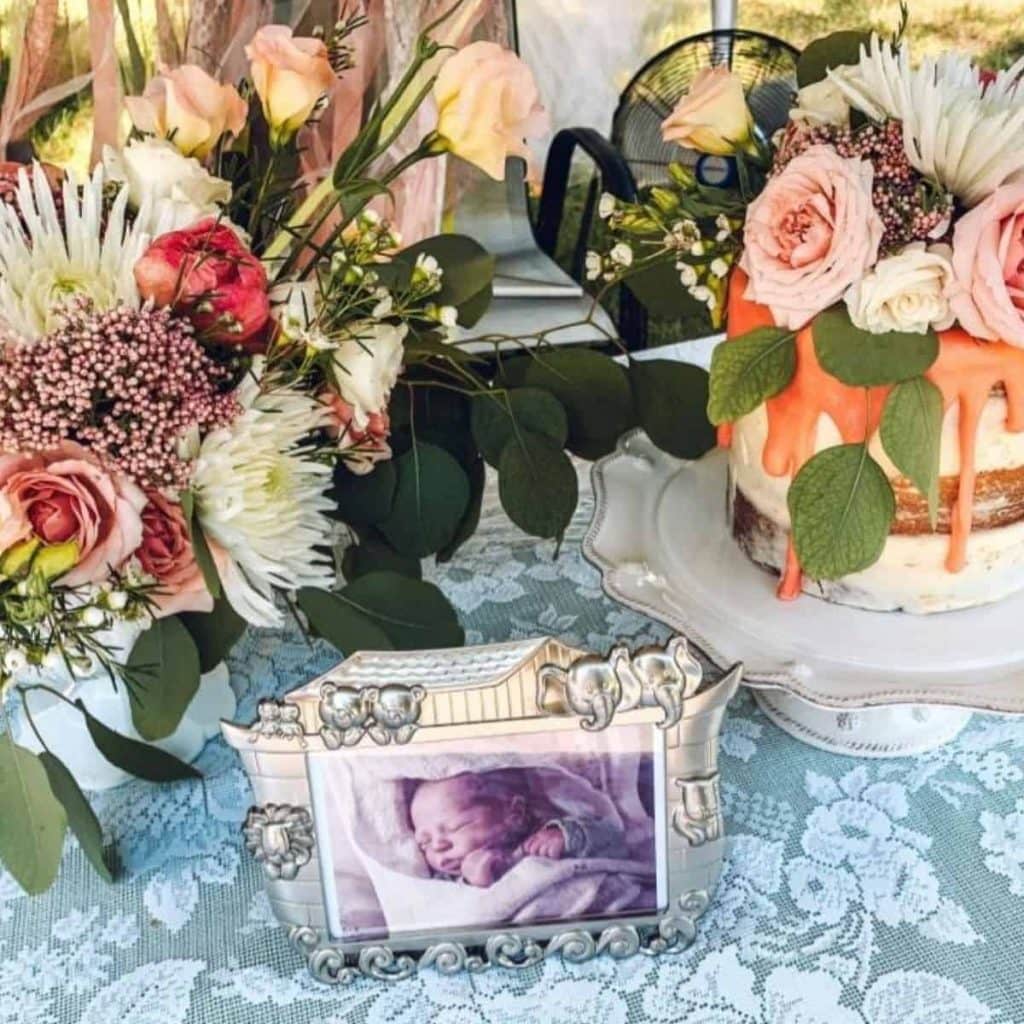flowers, cake, and photo of infant on a drive-by baby shower table