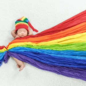 infant wearing a rainbow colored hat and wrapped in rainbow blanket