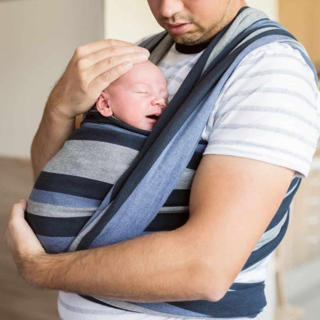 father holding newborn baby with baby wearing wrap