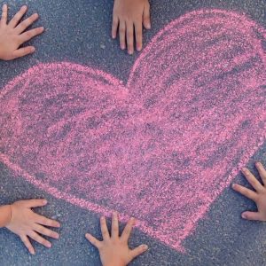 kids hands laid out on sidewalk next to a pink heart-shaped chalk outline