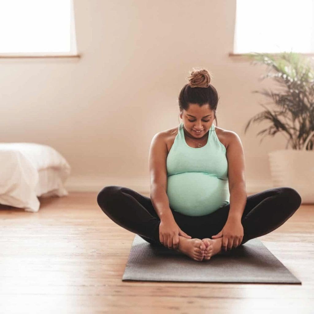 pregnant woman sitting on yoga mat doing stretches