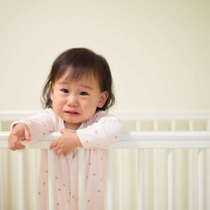 baby girl is crying while standing in her crib