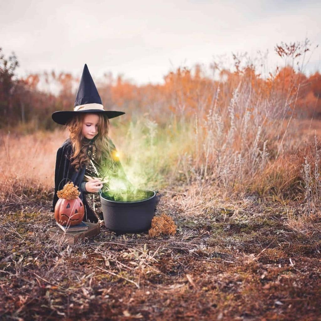 little girl dressed as a witch while playing with cauldron