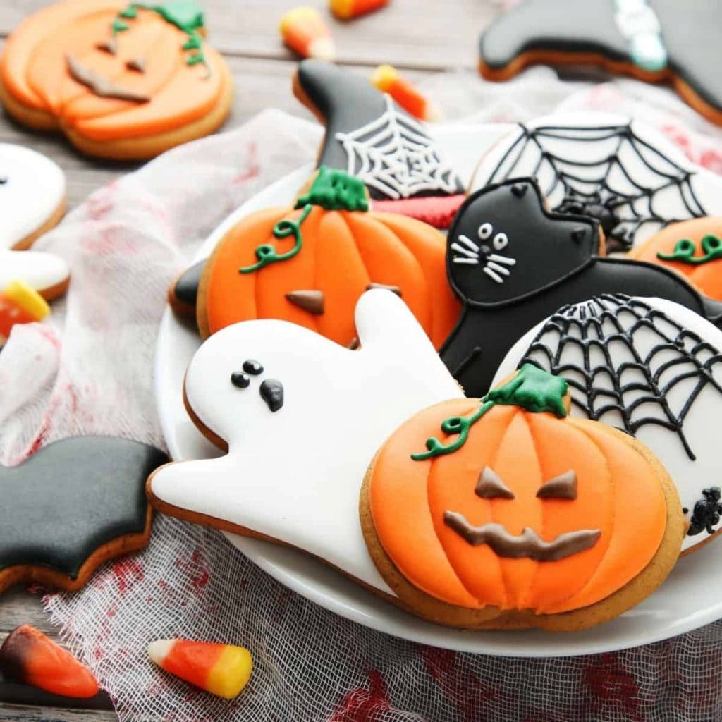 halloween cookies like ghosts, pumpkins, spiders, and black cats on a plate on a decorated table