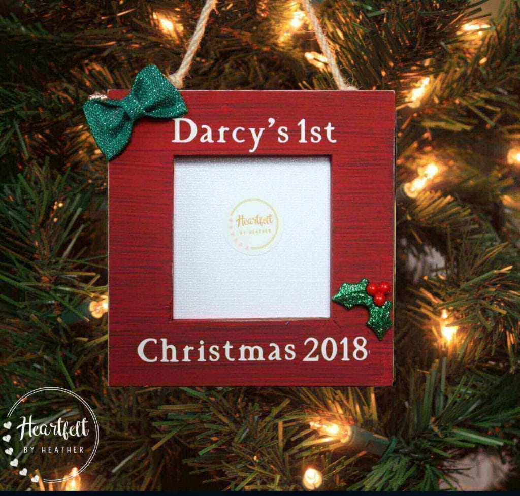 Red wooden square ornament hanging on Christmas tree that says Darcy's first Christmas with a small bow and an insert for a photo