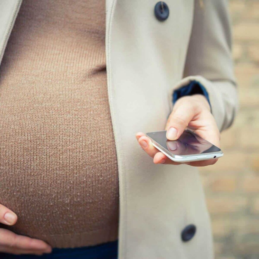 Woman holds her iphone and has one had on her pregnant belly.