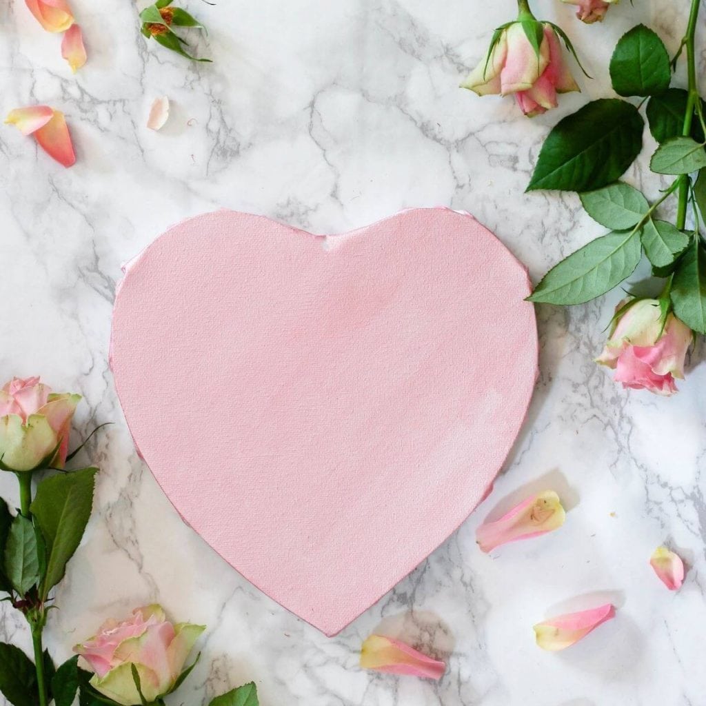 This photo shows a pink heart on top of a marble background, surrounded by pink roses.