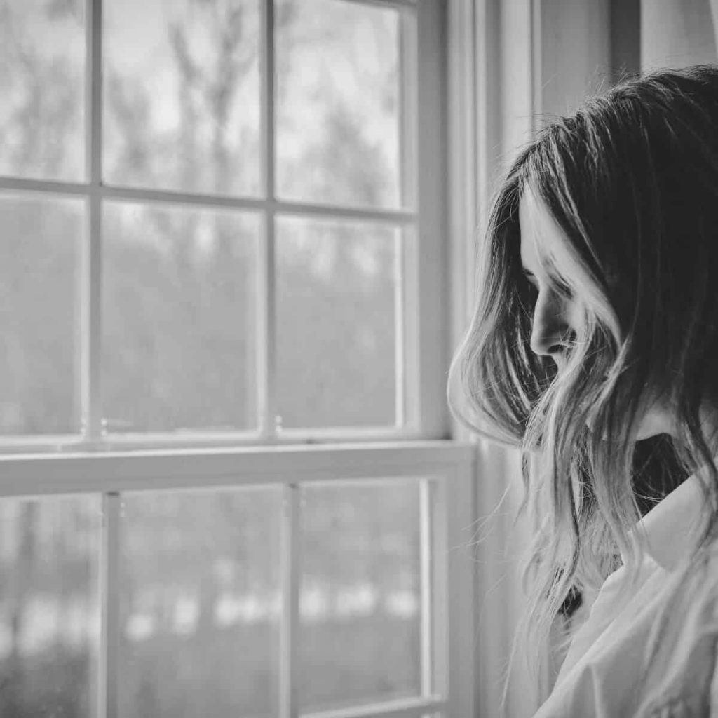 This black and white image shows a woman grieving by a window.