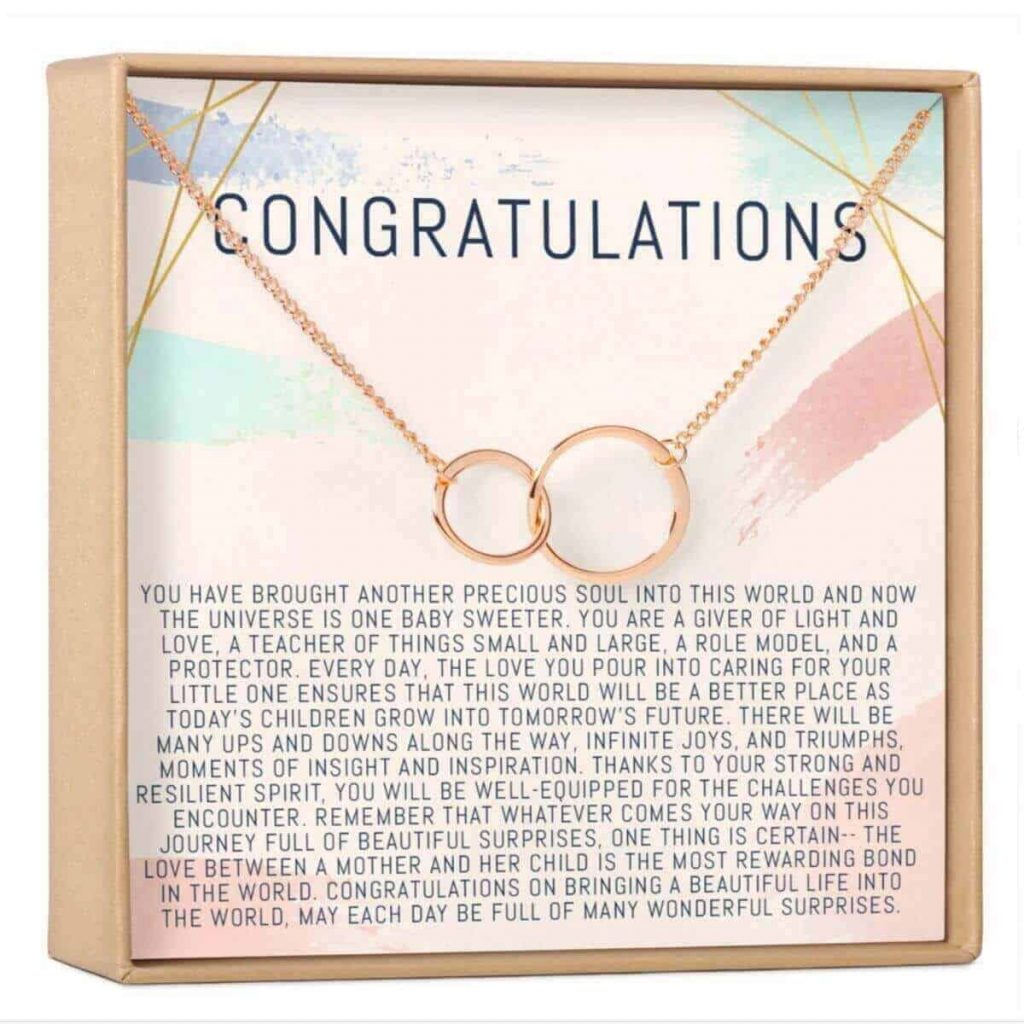 box with card that says congratulations and talks about the beauty of bringing a new baby into the world with a gold necklace chain hanging on the box with two interlocking gold circles on the necklace