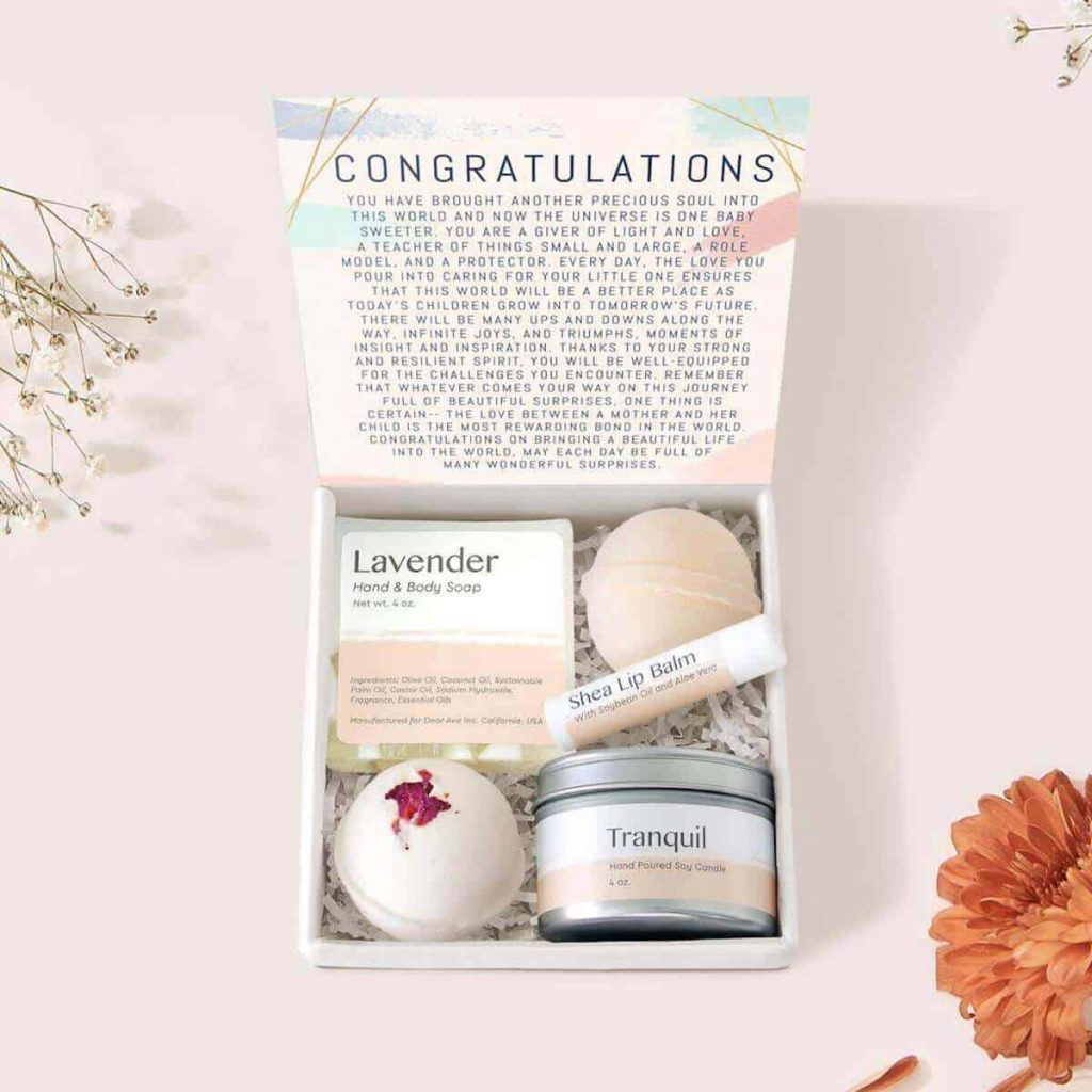 A gift box with an inspirational message that is open to show a bath bomb, lip gloss, soap, and a candle