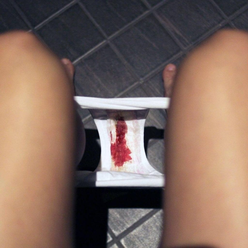 Photo from the angle of a woman's eyes looking down beyween her legs to see bright red blood on her white underwear