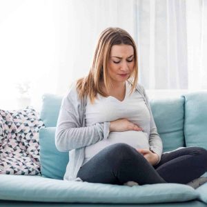 A photo of a woman sitting on the couch and she is holding her baby bump.
