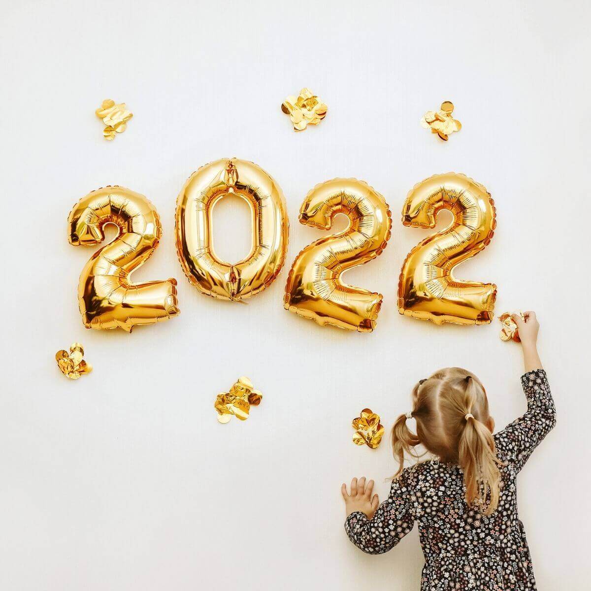 2022 in gold with little blonde girl in a black polka dot dress and pigtails putting a gold star near the numbers