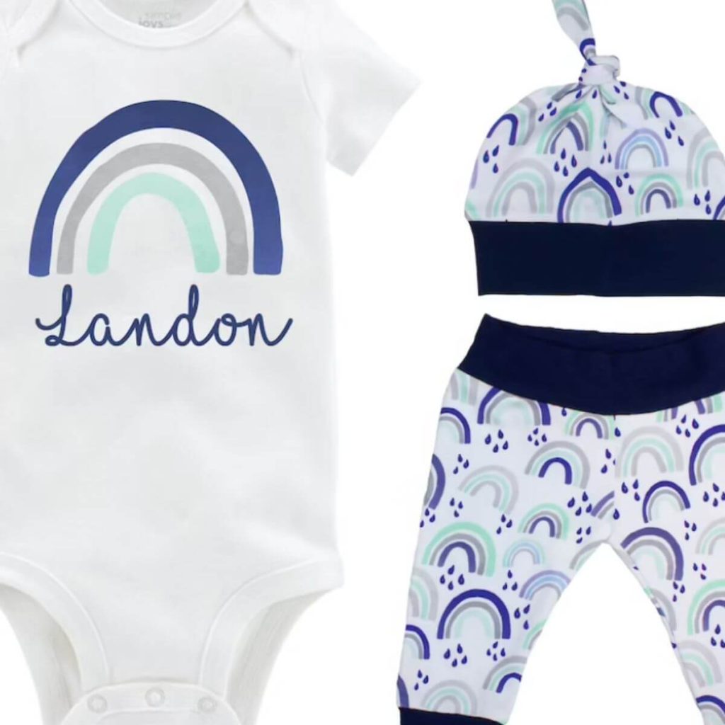 White customizable onesie with dark blue, light grey and light blue rainbow on the front Hat and pants that are white with dark blue trim with dark blue, light grey, and light blue rainbows