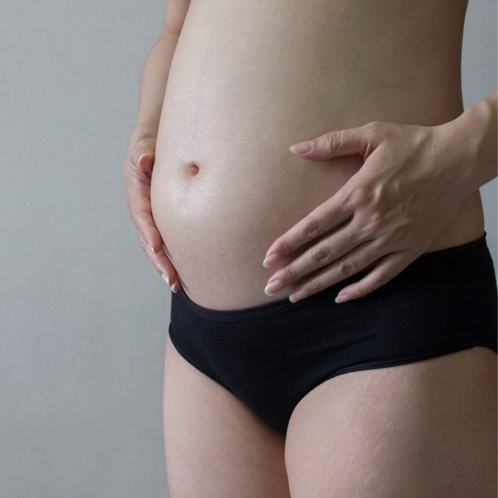 Caucasian woman's stomach down to her thighs wearing black underwear and her hands holding her belly