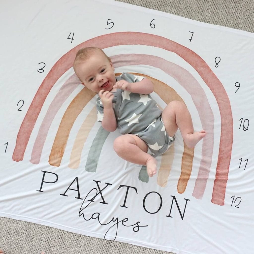 baby lying on a blanket with a big rainbow and numbers around the rainbow to show the different months of baby's age