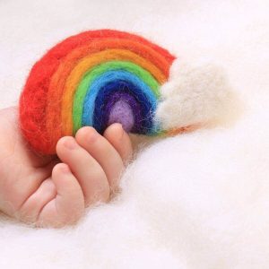 A baby's hand lays on top of white wool with a rainbow in hand with the colors red, dark orange, light orange, lime green, light blue, dark blue, violet, and light purple with a white cloud on the bottom right of the rainbow