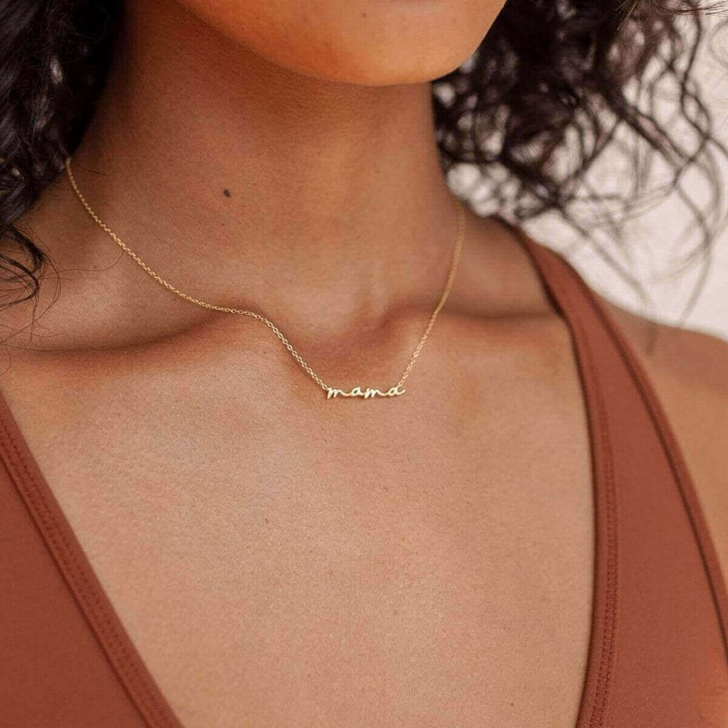Woman's neckline with a thin gold chain necklace with the word mama on it