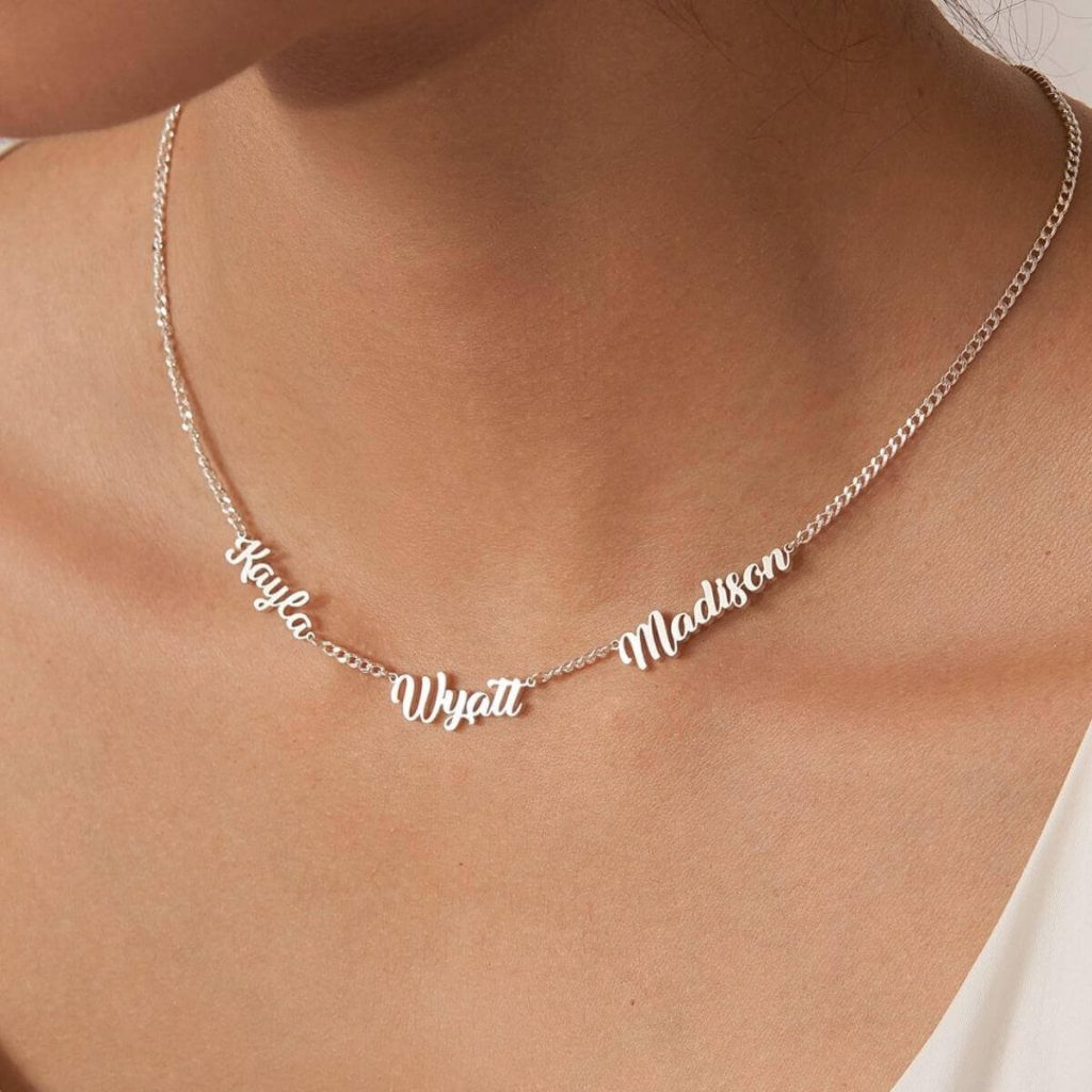 A woman's neckline with a silver chain necklace wit hthe names Kayla, Wyatt, and Madison on it.